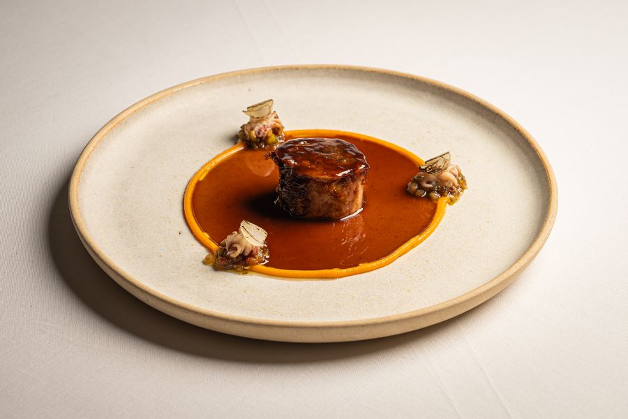 Carne glaseada sobre un cordón de salsa naranja, en plato blanco